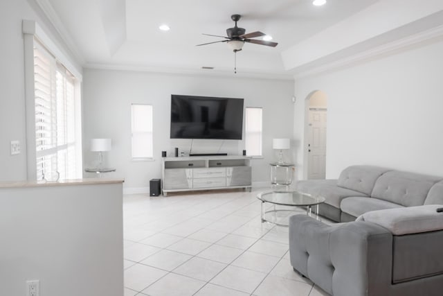 living room featuring arched walkways, light tile patterned floors, a raised ceiling, and ornamental molding