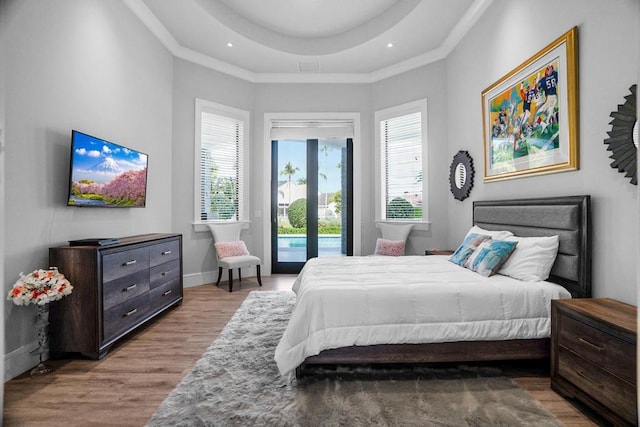 bedroom with access to exterior, crown molding, light hardwood / wood-style flooring, and a raised ceiling