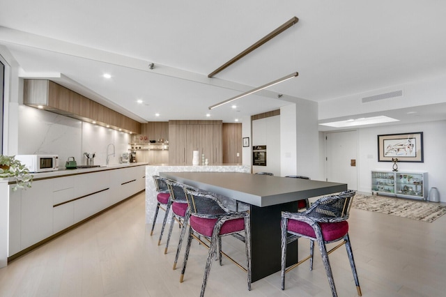 kitchen featuring visible vents, white microwave, white cabinetry, modern cabinets, and a kitchen bar