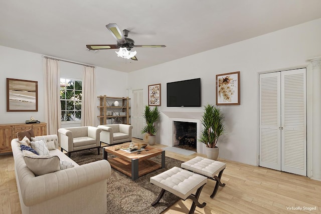 living area with a fireplace with flush hearth, light wood finished floors, and ceiling fan