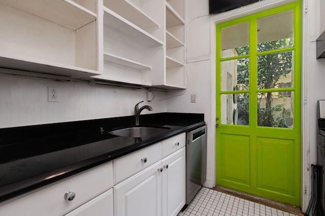 kitchen with a sink, white cabinets, stainless steel dishwasher, open shelves, and dark countertops