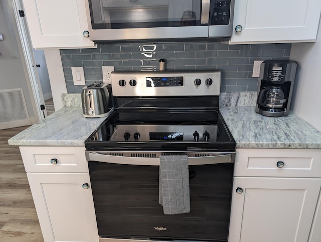 kitchen featuring stainless steel appliances, tasteful backsplash, light stone countertops, and white cabinets