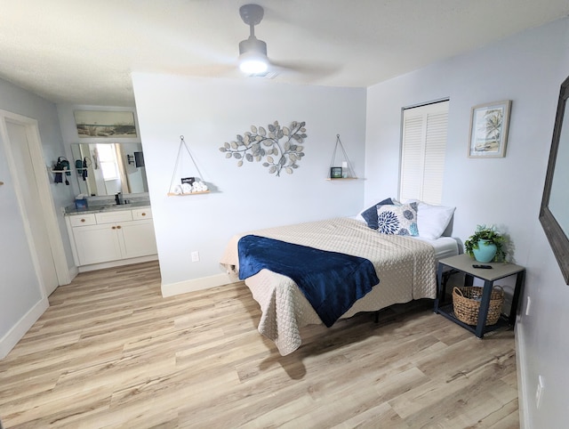 bedroom featuring ceiling fan, ensuite bath, sink, and light hardwood / wood-style flooring