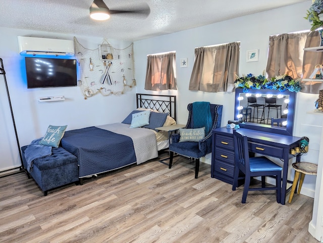 bedroom with a wall mounted air conditioner, a textured ceiling, and light wood-type flooring