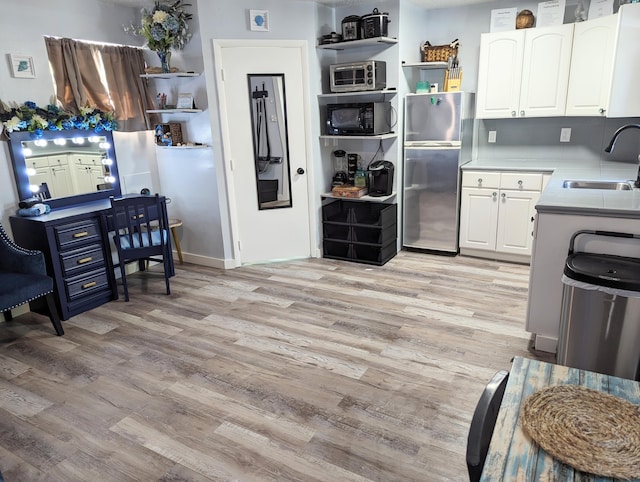 kitchen featuring white cabinetry, sink, light hardwood / wood-style floors, and stainless steel refrigerator