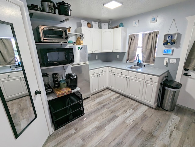 kitchen with sink, stainless steel fridge, white cabinets, a textured ceiling, and light hardwood / wood-style flooring