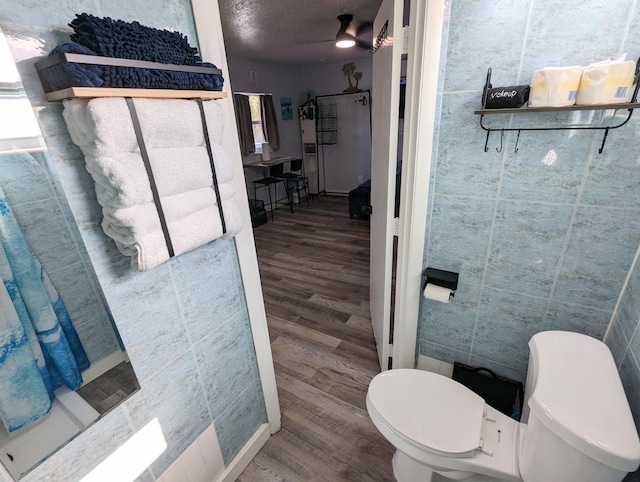 bathroom with wood-type flooring, tile walls, a textured ceiling, and toilet