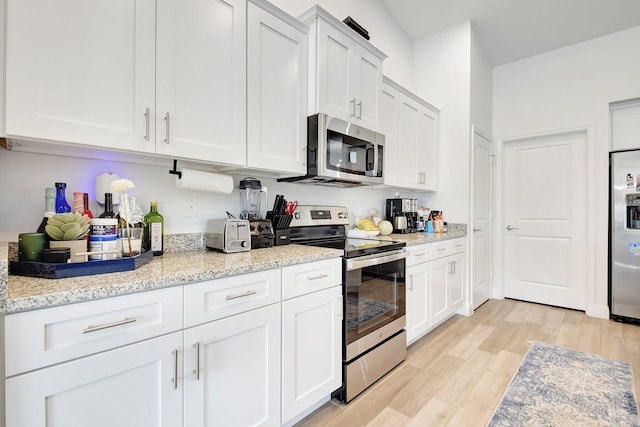 kitchen with white cabinetry, appliances with stainless steel finishes, light hardwood / wood-style floors, and light stone counters