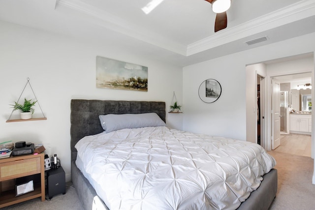 carpeted bedroom with a raised ceiling, ornamental molding, ensuite bathroom, and ceiling fan