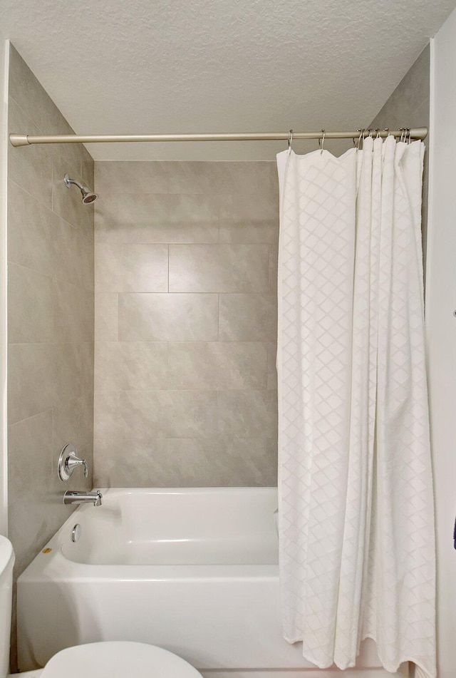 bathroom featuring toilet, shower / tub combo, and a textured ceiling