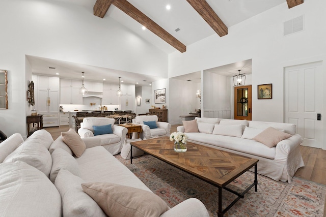 living room with beamed ceiling, a notable chandelier, high vaulted ceiling, and light wood-type flooring