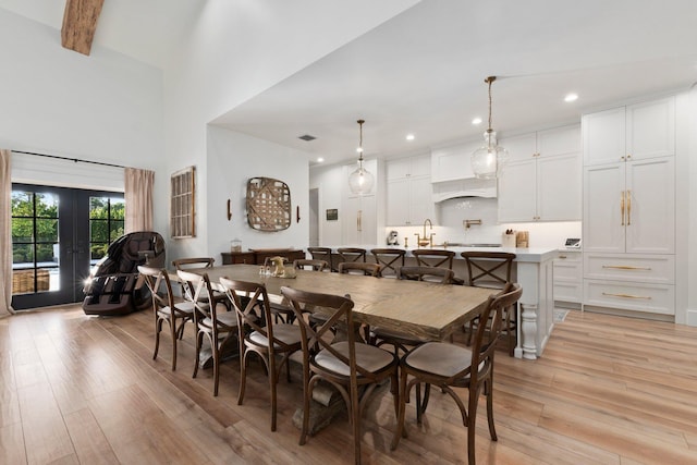 dining area with a towering ceiling, beamed ceiling, sink, light hardwood / wood-style floors, and french doors