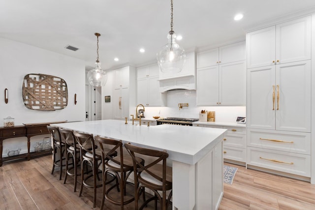 kitchen featuring light hardwood / wood-style flooring, a kitchen island with sink, light stone counters, white cabinets, and decorative light fixtures