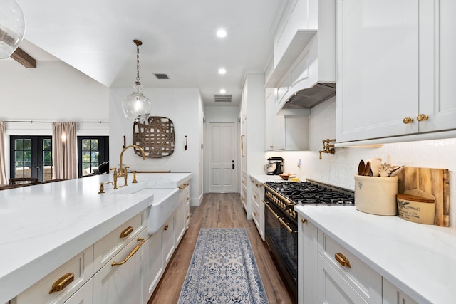 kitchen featuring sink, light stone counters, custom range hood, range with two ovens, and white cabinets