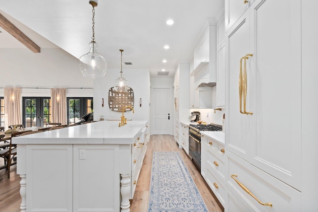 kitchen featuring white cabinets, double oven range, hanging light fixtures, and a large island with sink