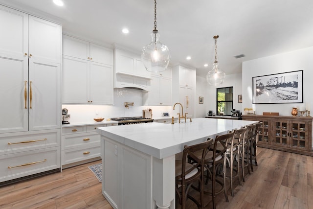 kitchen featuring a breakfast bar, white cabinetry, light stone counters, a center island with sink, and decorative light fixtures