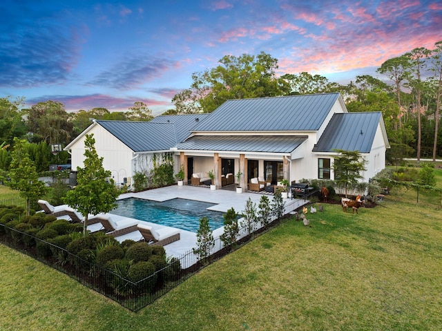 back house at dusk featuring a fenced in pool, outdoor lounge area, a patio area, and a lawn