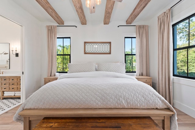 bedroom featuring beamed ceiling, ensuite bath, and light hardwood / wood-style flooring