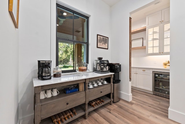 bar with wine cooler, white cabinets, and light hardwood / wood-style floors