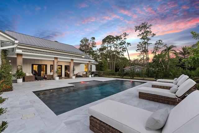 pool at dusk featuring an outbuilding, a patio area, and outdoor lounge area