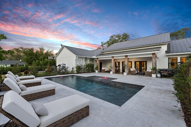 pool at dusk with an outdoor living space, an outdoor structure, and a patio area