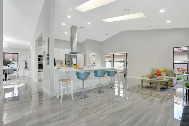 kitchen featuring kitchen peninsula, a skylight, white cabinets, a kitchen bar, and stainless steel fridge with ice dispenser