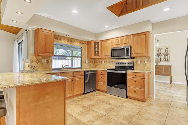 kitchen featuring appliances with stainless steel finishes, glass insert cabinets, a peninsula, light stone countertops, and a sink