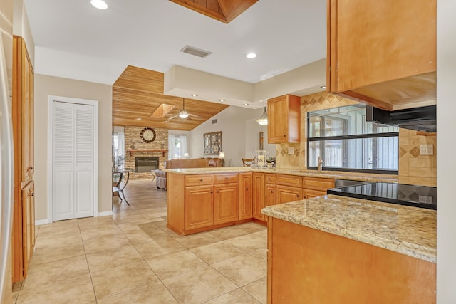 kitchen featuring a peninsula, a sink, visible vents, open floor plan, and a brick fireplace