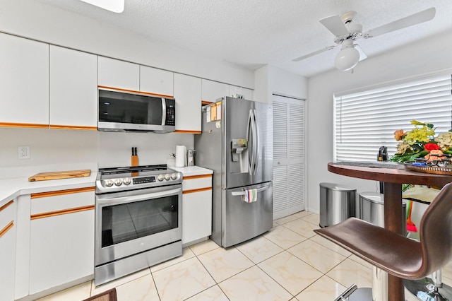 kitchen with light tile patterned flooring, a textured ceiling, appliances with stainless steel finishes, ceiling fan, and white cabinets