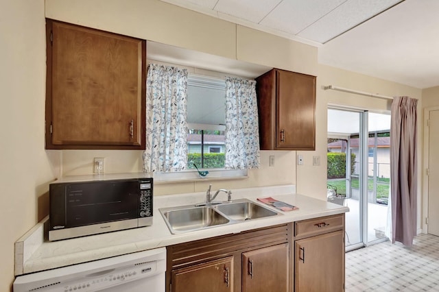 kitchen with light countertops, stainless steel microwave, white dishwasher, and a sink