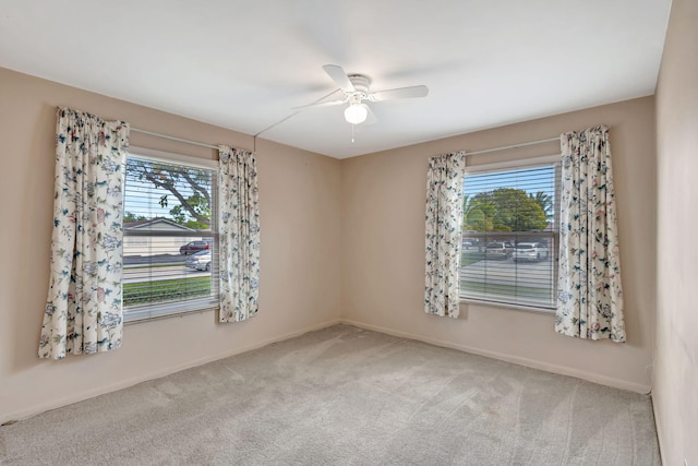 carpeted spare room featuring a healthy amount of sunlight, ceiling fan, and baseboards