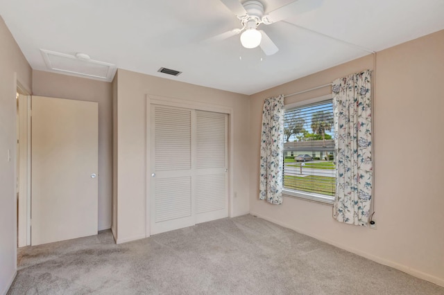 unfurnished bedroom with attic access, visible vents, a ceiling fan, carpet flooring, and a closet