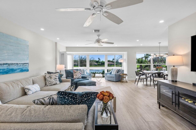 living room with ceiling fan with notable chandelier and light hardwood / wood-style flooring