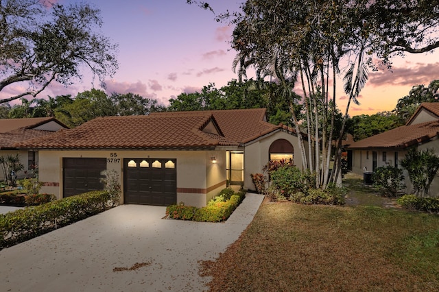 mediterranean / spanish home with driveway, a tiled roof, an attached garage, a front lawn, and stucco siding