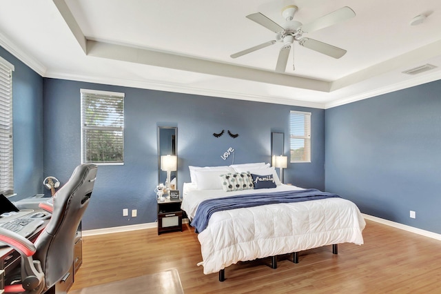 bedroom with multiple windows, a tray ceiling, and light wood-type flooring