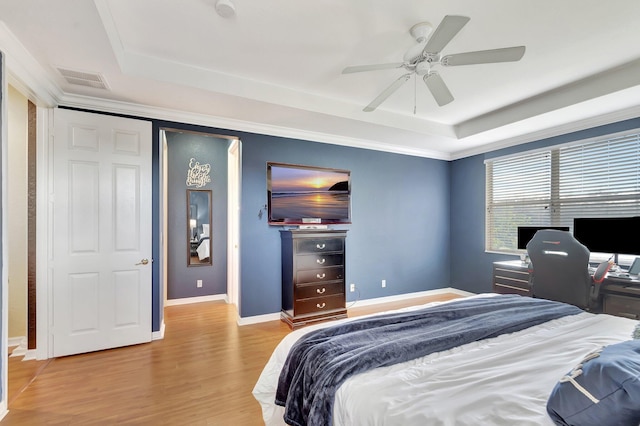 bedroom featuring ceiling fan, ornamental molding, a tray ceiling, and light hardwood / wood-style floors