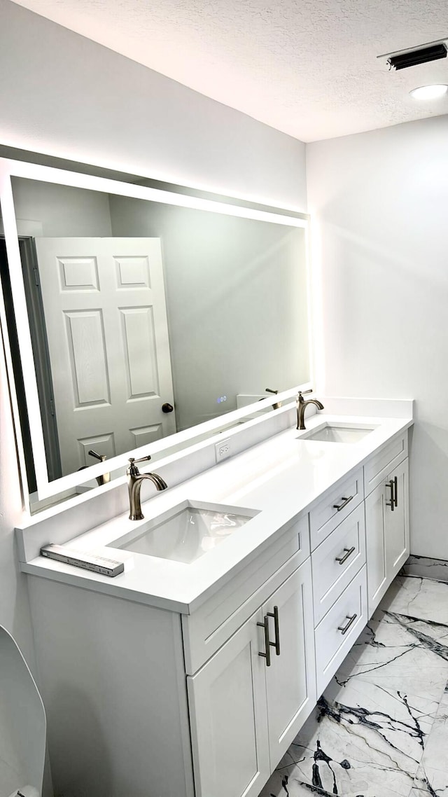 1001 Cape Cod Ter, Greenacres, FL 33413 - bathroom featuring marble look tiles, double vanity, and a textured ceiling