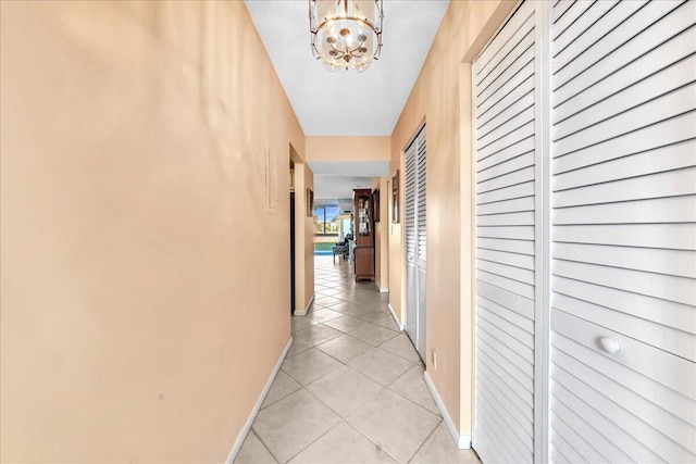 corridor with light tile patterned floors, a notable chandelier, and a textured ceiling