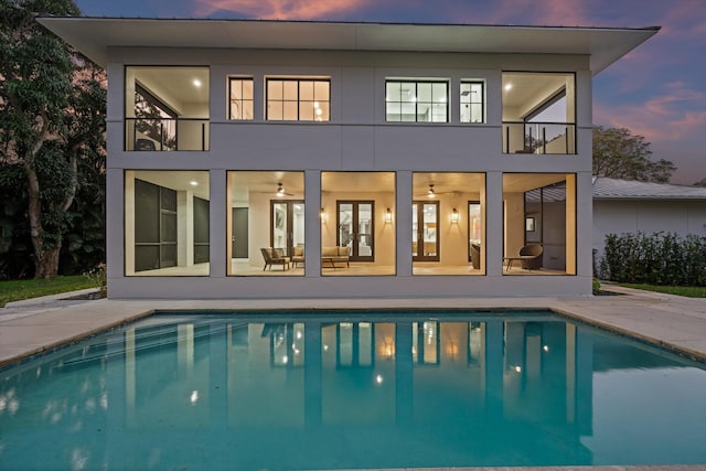 back house at dusk with french doors, a balcony, an outdoor living space, and a patio area