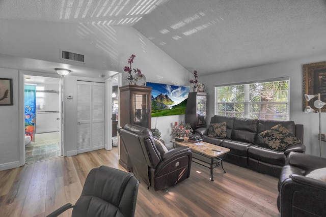 living room featuring vaulted ceiling, a textured ceiling, and light hardwood / wood-style flooring