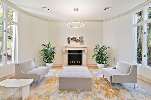 sitting room featuring ornamental molding, a healthy amount of sunlight, a high end fireplace, and light wood-type flooring