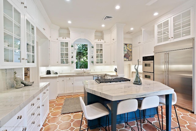 kitchen with appliances with stainless steel finishes, white cabinetry, sink, a center island, and light stone countertops