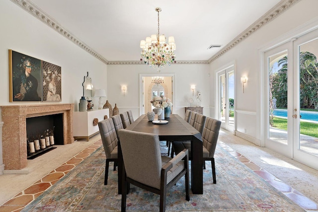 dining space with a premium fireplace, crown molding, a notable chandelier, and french doors