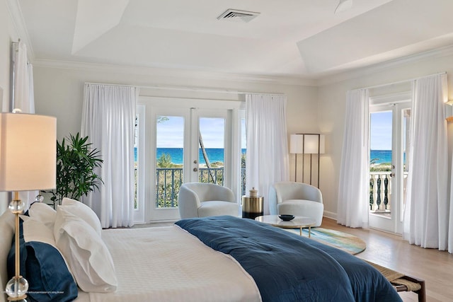 bedroom featuring multiple windows, access to outside, a raised ceiling, and a water view