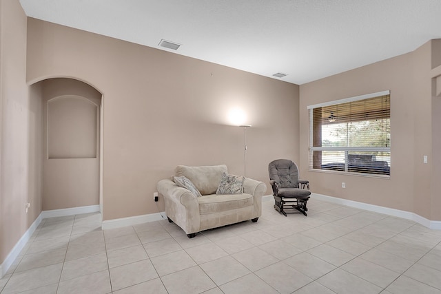 living area featuring light tile patterned floors, baseboards, visible vents, and arched walkways