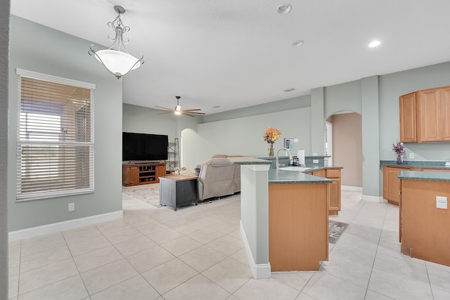 kitchen with arched walkways, open floor plan, light brown cabinetry, pendant lighting, and a sink