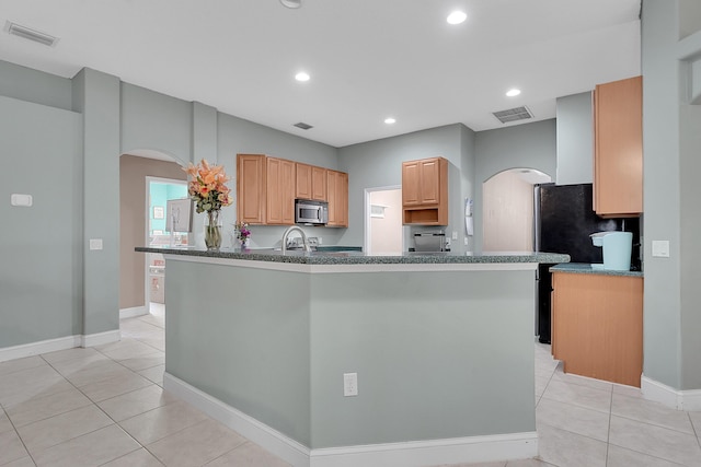 kitchen featuring visible vents, stainless steel microwave, arched walkways, and light tile patterned flooring