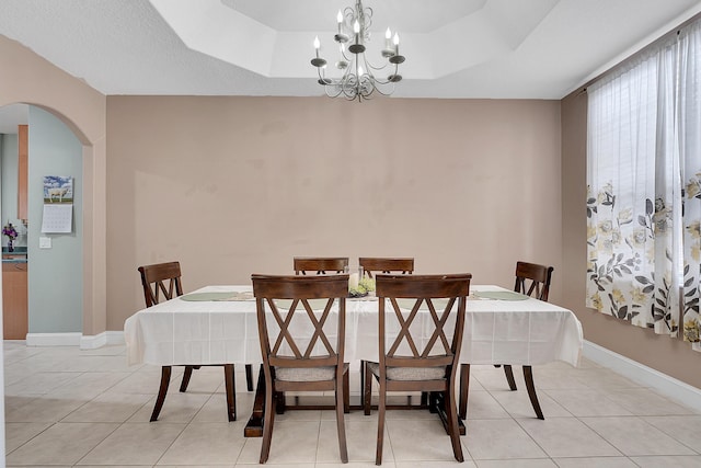 dining area featuring an inviting chandelier, baseboards, arched walkways, and a raised ceiling