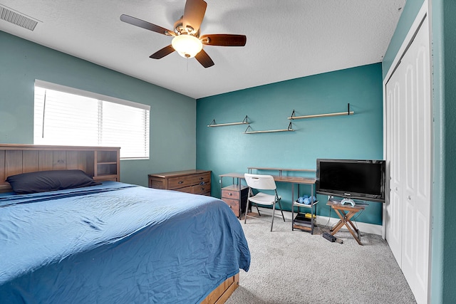 carpeted bedroom featuring a ceiling fan, a closet, visible vents, and a textured ceiling