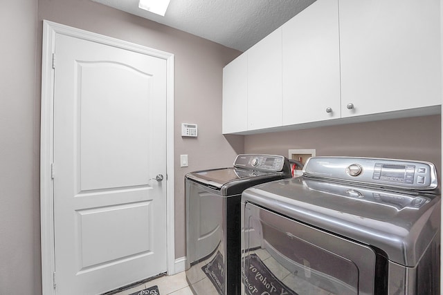 laundry room with light tile patterned floors, cabinet space, a textured ceiling, and separate washer and dryer